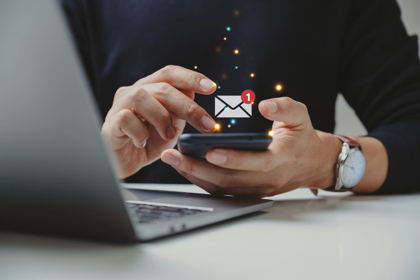 homme devant son ordinateur qui reçoit un mail sur son téléphone